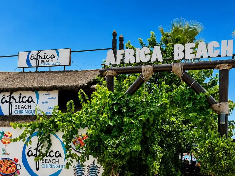 Entrada del Chiringuito África Beach en el paseo marítimo de Estepona, con el rótulo y la vegetación